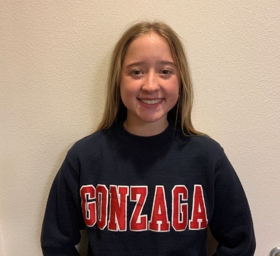 Jade, a current student, smiling against a blank wall. She is wearing a navy crewneck sweatshirt with GONZAGA in red letters. 