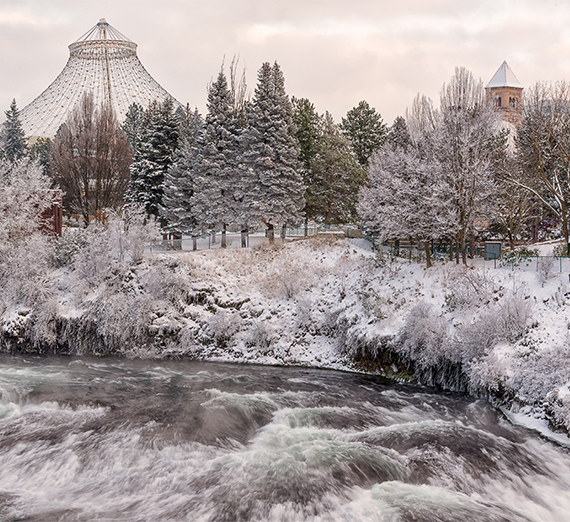 A snowy view of downtown Spokane, showing the river, pavilion, and clock tower in the park.