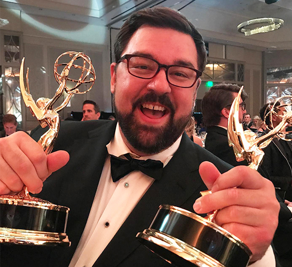 Man with glasses, wearing a black suit and bow tie, smiling and holding his two Southeast Emmy Awards. 