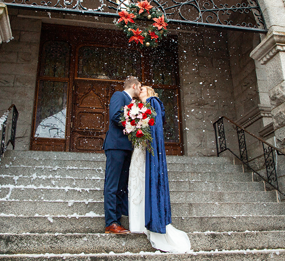 Two people kiss on church steps while snow falls.