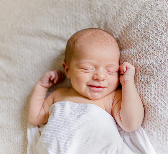 A baby smiles while wrapped in a white blanket.