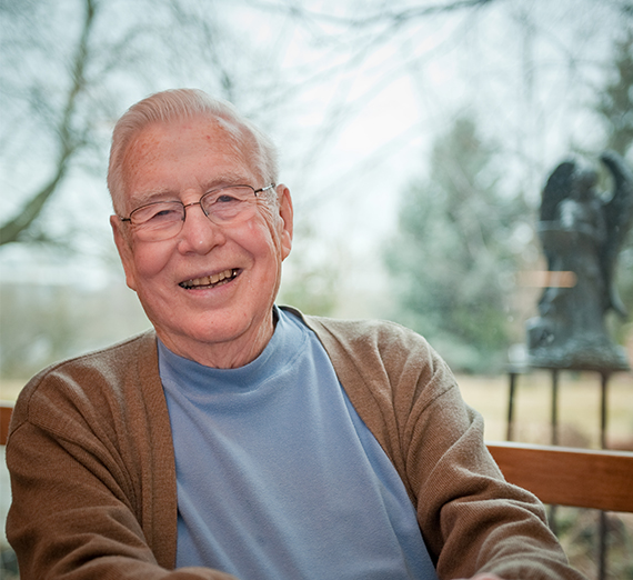 Fr. Costello smiles in front of some trees. 