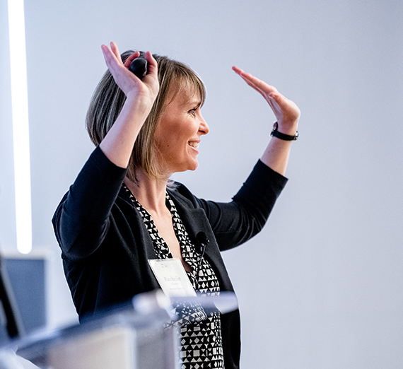 woman at podium smiling with hands up