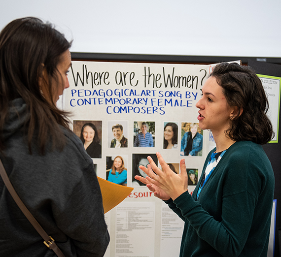 Two women stand in front of a presentation board. They are talking with each other.