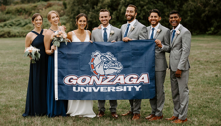 Bride and groom pose with bridal party behind Gonzaga University flag. 