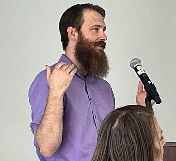 English professor Chase Bollig speaks into a microphone in front of a white board