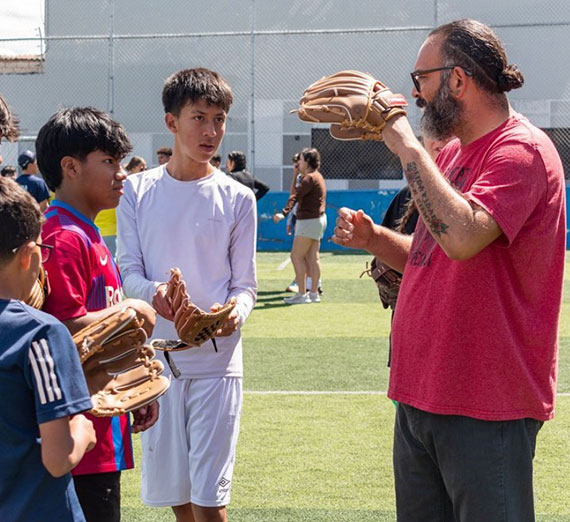 Three young boys in Ecuador look at a coach holding up a baseball glove