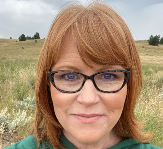 A woman with red hair and glasses looks into the camera