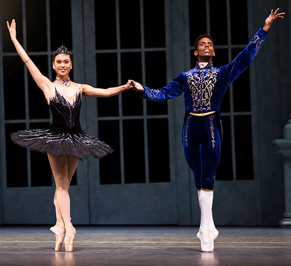 Two ballet dancers stand en pointe while holding hands