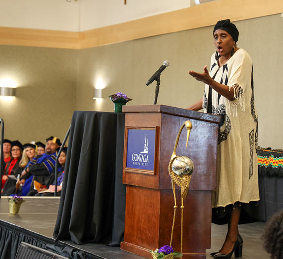 A woman stands speaking at a podium with a Gonzaga logo on the front