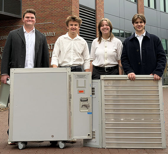 Four students stand in front of a set of large metal boxes