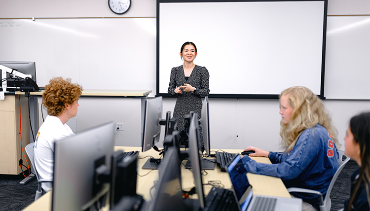 female instructor in front of class with students on computers