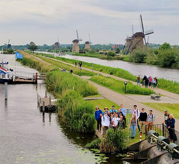 Students smile in front of Kinderdijk windmills. 