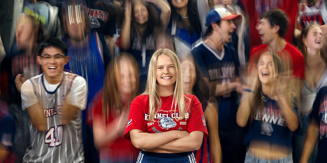 A woman stands with her arms crossed among cheering students