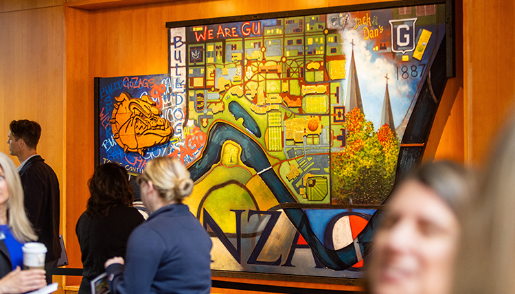 Photo of a painting hanging on the wall with people talking in front of it. 