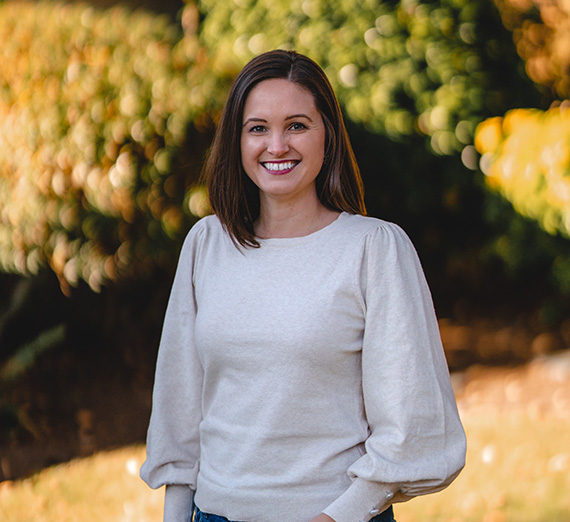 Brown haired woman standing outside in a white blouse. Carrie DeDonker, ORGL alumna