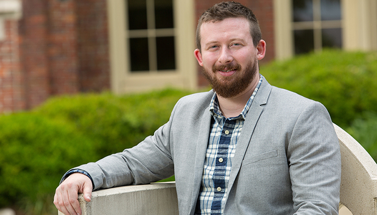 A man in a gray jacket sits on a bench outside