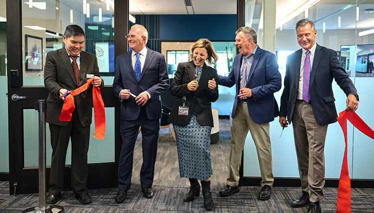 Five people stand holding pieces of a large red ribbon