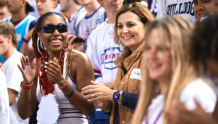 A woman in sunglasses claps in the crowd of a basketball game