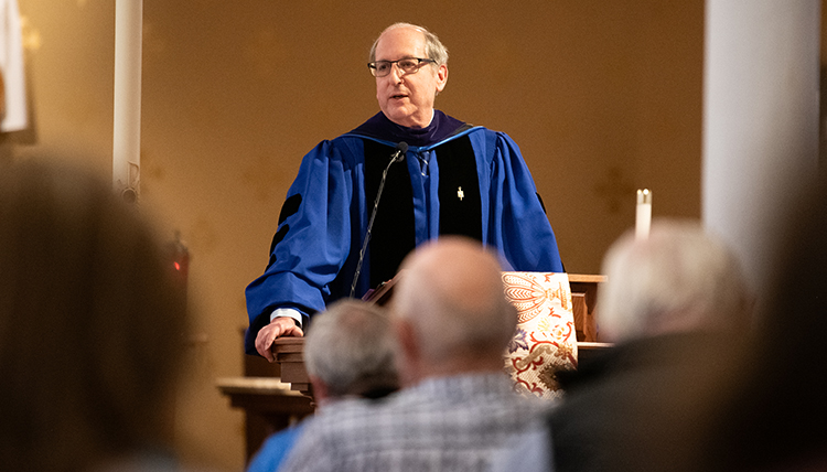 A man in a blue robe stands at a podium in front of a crowd.