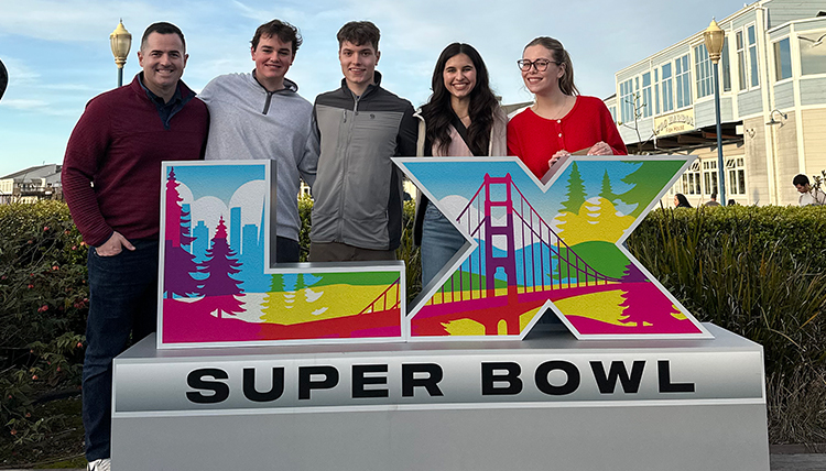 five people stand behind a sign saying Super Bowl