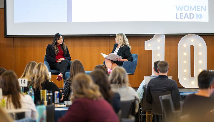 Two women converse on a stage while a seated audience listens