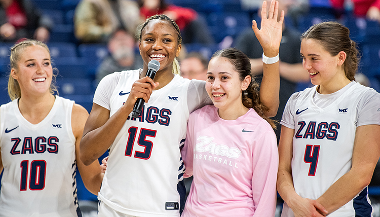 Four women basketball players are celebrated on Senior Night, one holding a microphone and talking