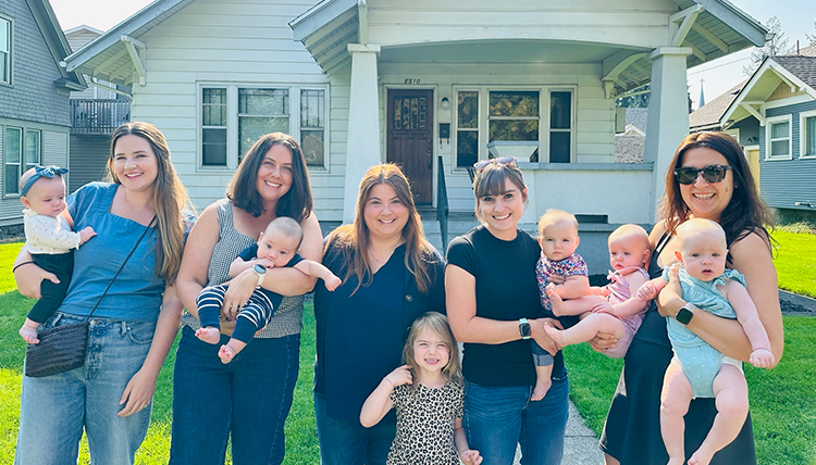 A group of women and babies in front of a house.