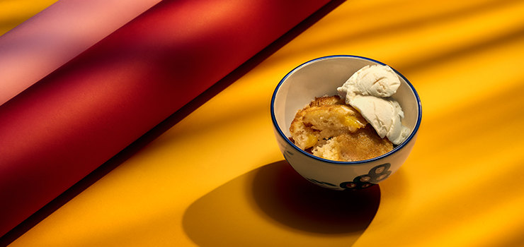 Peach cobbler in a bowl on a yellow backdrop.