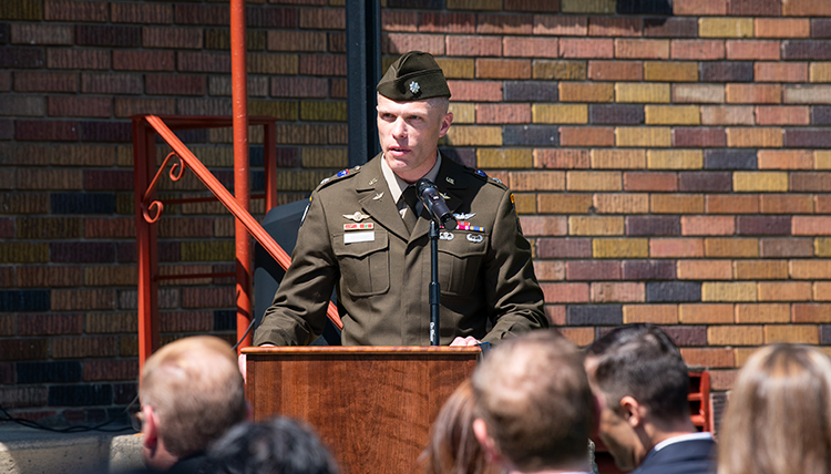 Man in green military uniform speaks at a podium.