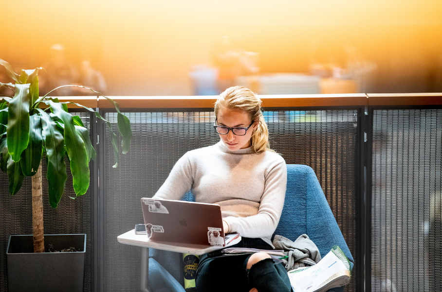 Student studying on laptop in a blue chair.