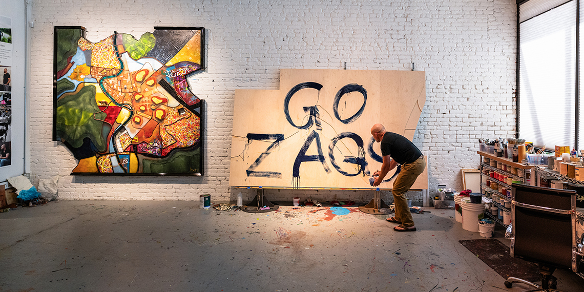 Artist Ben Joyce painting Go Zags on a canvas next to a completed work