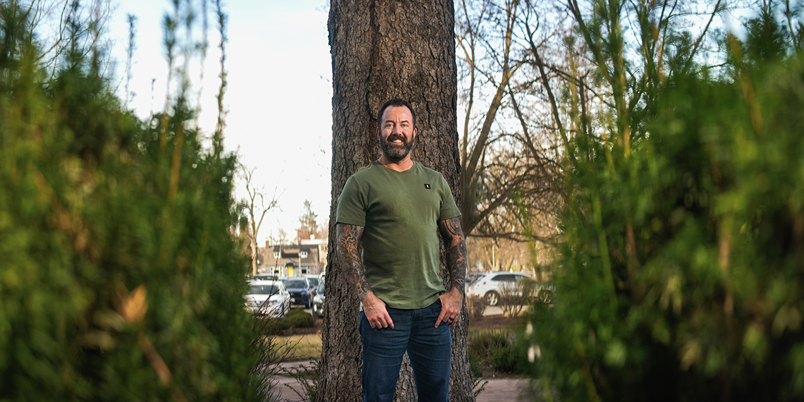 Dan Cummins stands in front of a tree trunk