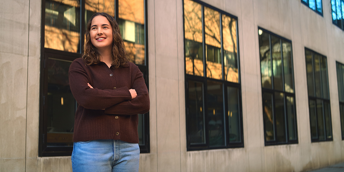 A woman stands with her arms crossed in front of some windows