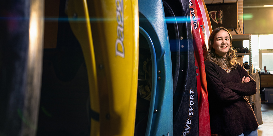 A woman stands alongside several kayaks