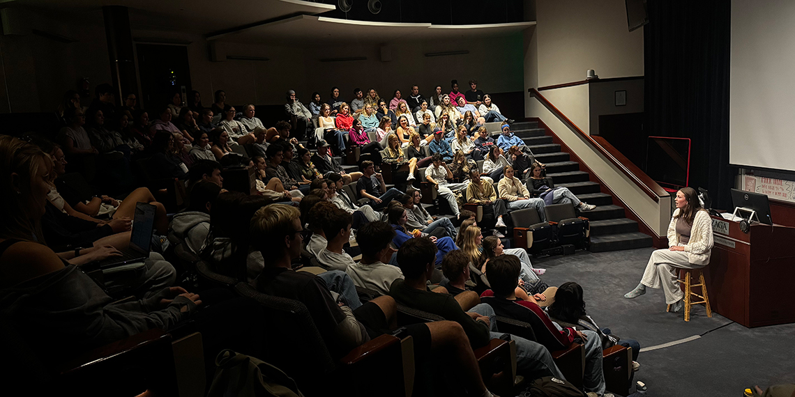 A woman on a stool speaks to a room full of seated people