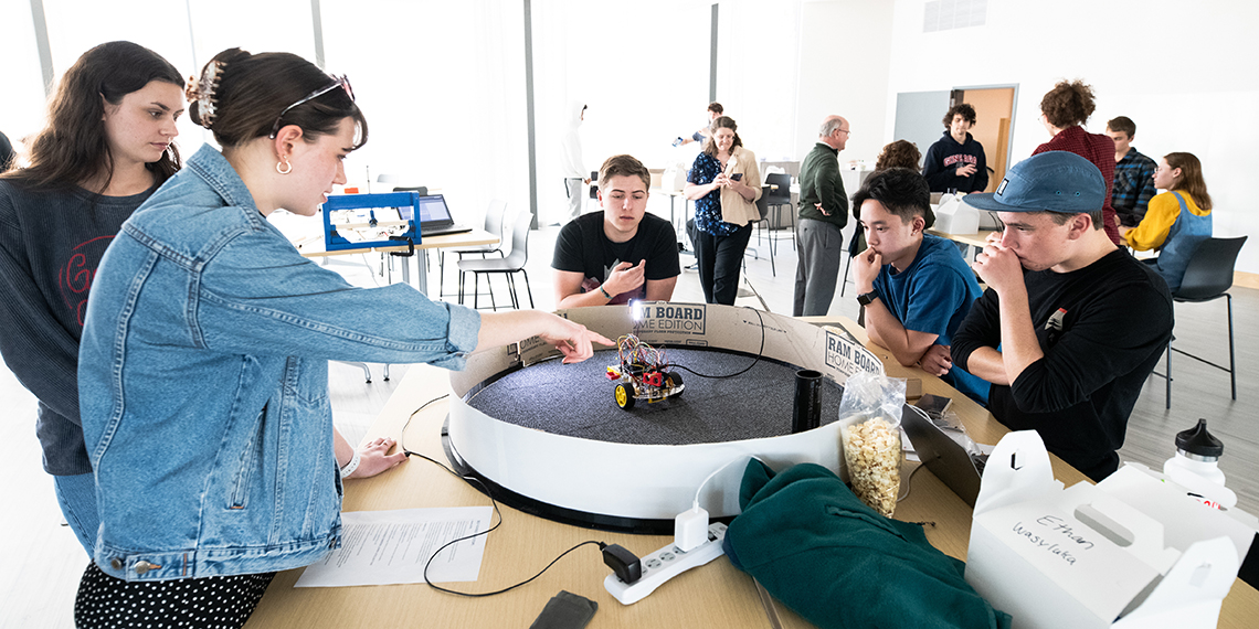 A group of students gathered around a table with a small robot on it