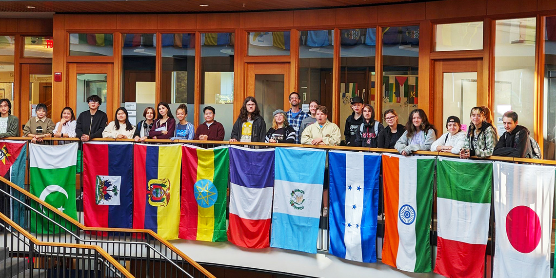 Wesley Schantz stands with students beside international flags in Gonzaga's Hemmingson Center. 