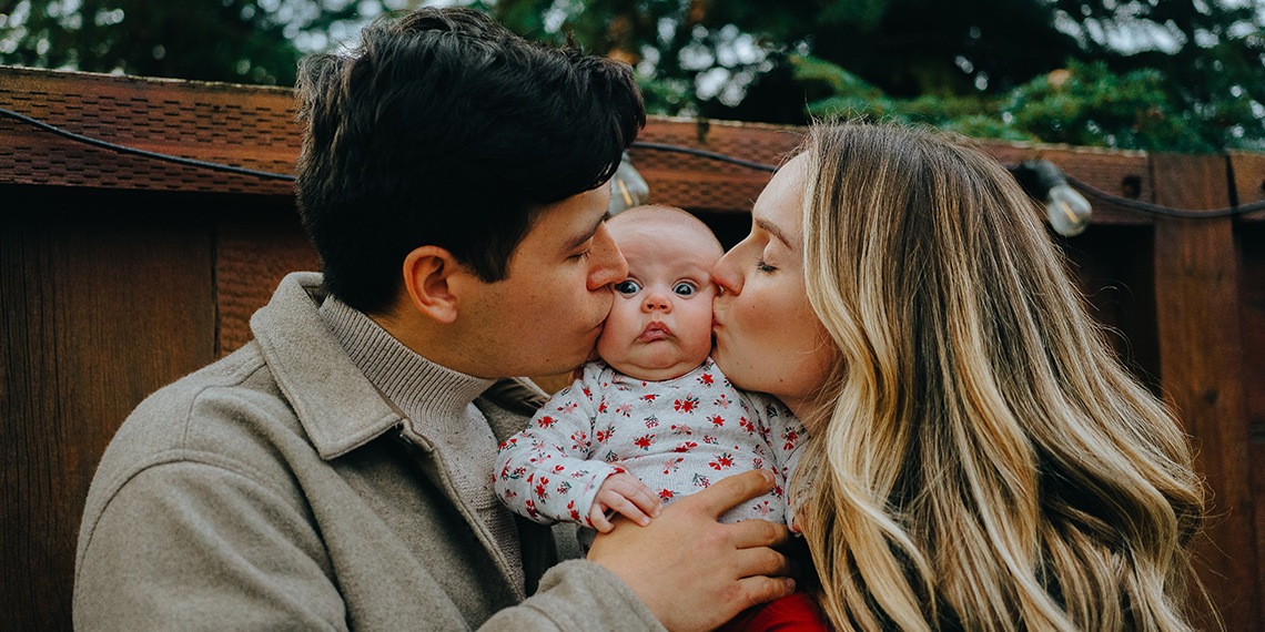 Mom and dad kissing a baby's cheek.