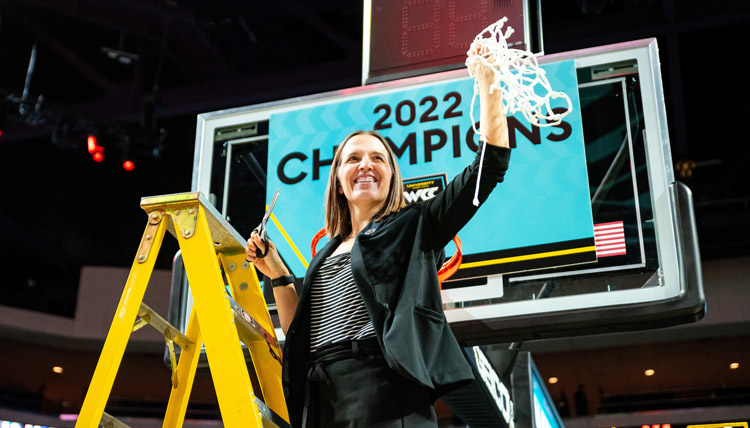 Head Women's Basketball coach Lisa Fortier on a ladder holding the net after winning the 2022 WCC Championship