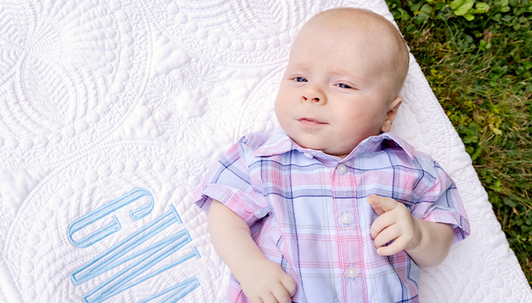 A baby on a blanket with initials embroidered on it.