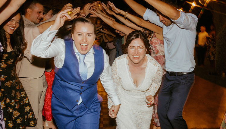 Two people running and smiling under a tunnel of other people.