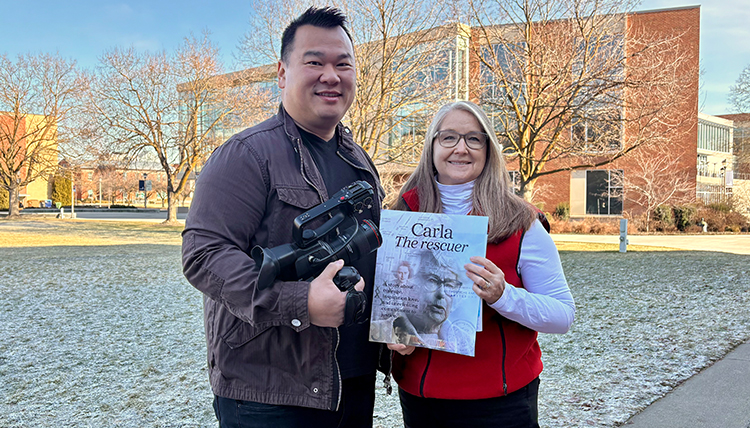 Clement Lye stands holding a camera next to Kristine Hoover holding a magazine. 