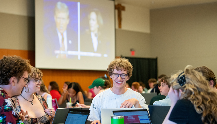 students sitting at tables watching the presidential debate on big screens