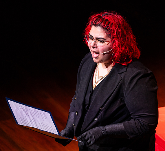 A woman with red hair holding a script and speaking