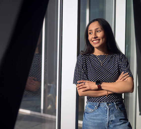 A woman stands with her arms crossed next to a window
