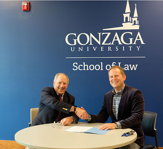 Image of GU Law School Dean Jacob Rooksby shaking hands with Jim Bamberger in front of Gonzaga School of Law Sign. 
