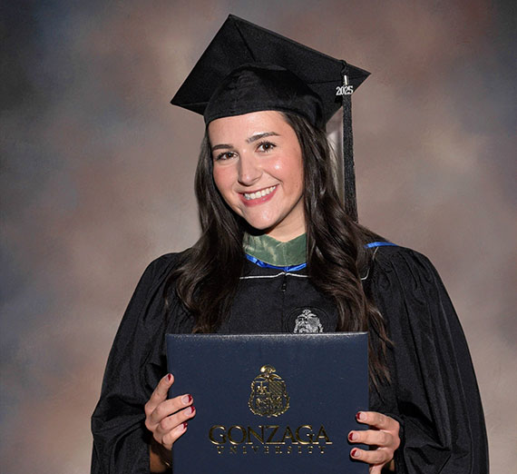 MASAA alum, Daphne Succic wearing graduation cap and gown and holding Gonzaga diploma folder 