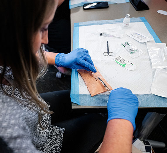 A graduate school nurse practicing sutures on synthetic skin.