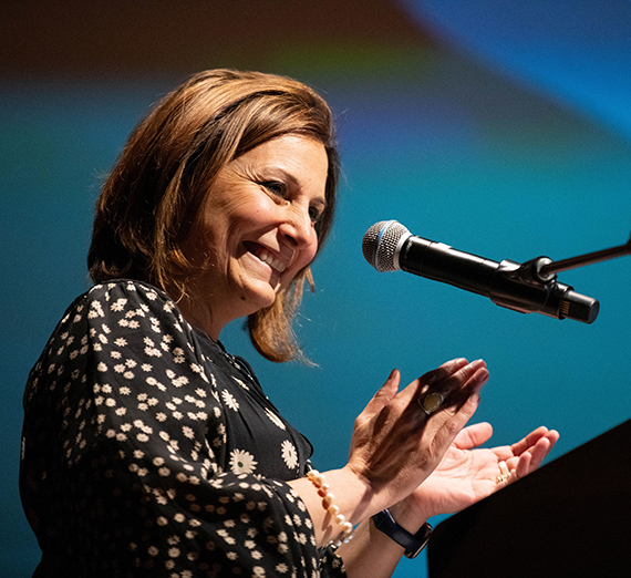 A smiling woman claps her hands standing near a microphone